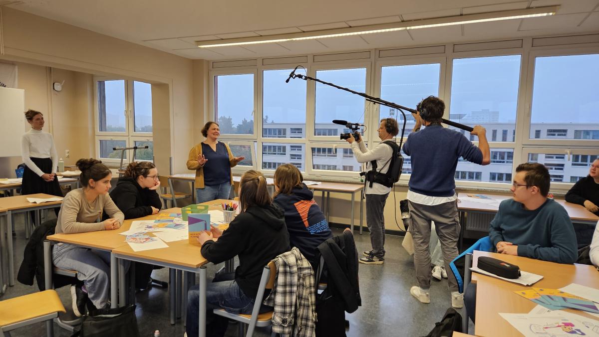 Eine junge Frau wird gefilmt, während sie zu jungen Leuten in einem Klassenraum spricht.