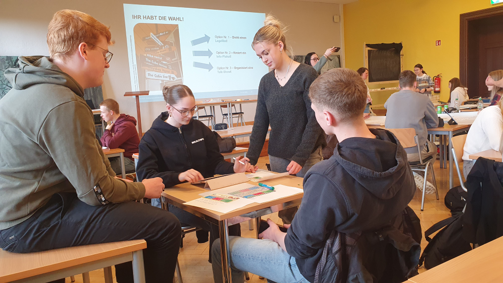 Eine Gruppe Jugendlicher sitzt und steht gemeinsam an einem Tisch und erarbeitet eine Präsentation.